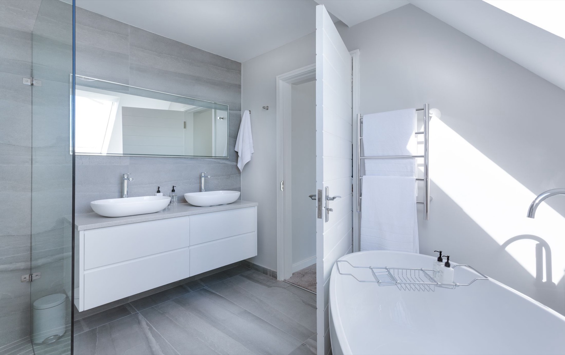 A calm, modern bathroom finished in pale grey large-format tiling with twin basins and a freestanding bath
