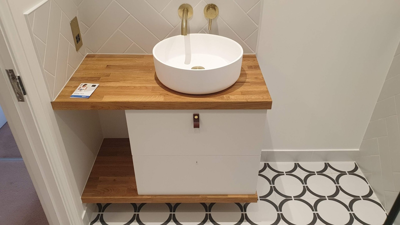 A small downstairs cloakroom built around a solid oak top and a round countertop basin, over a monochrome geometric floor tile.