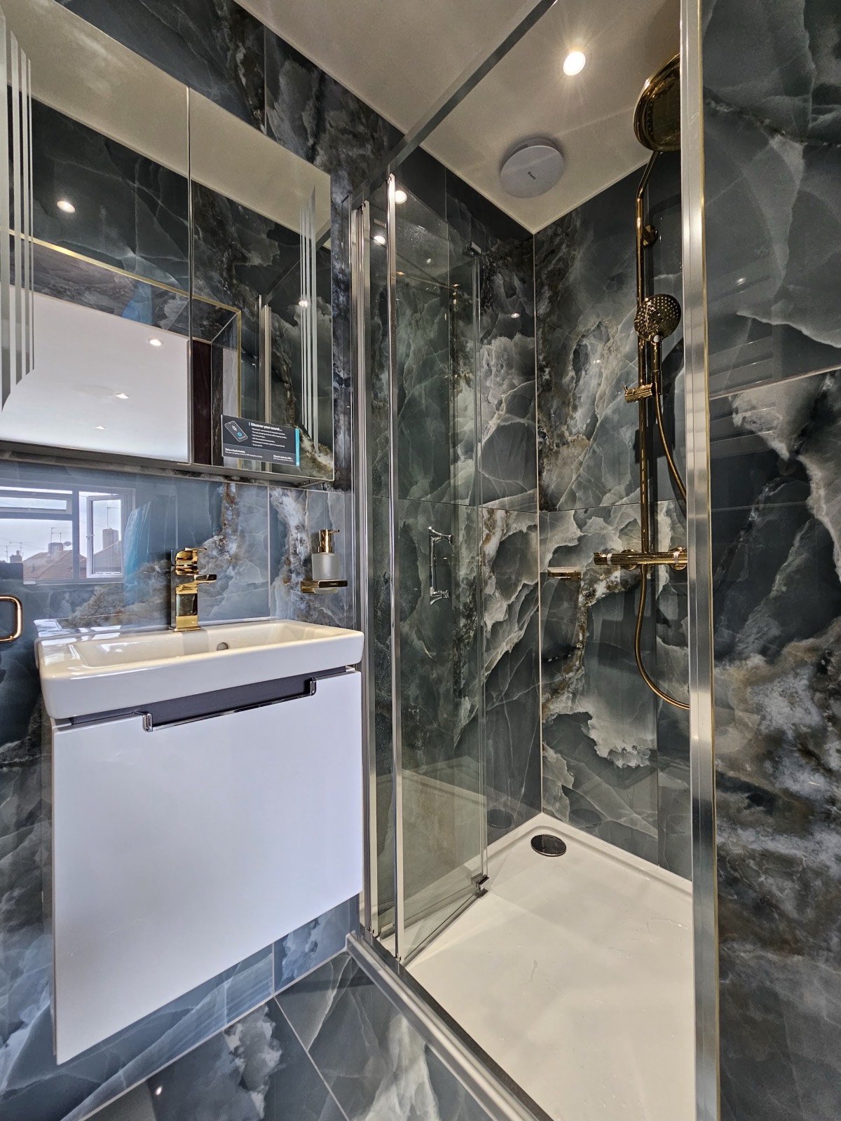 Dark onyx-effect porcelain floor to ceiling, gold brassware and a wall-hung basin unit — a small room made to feel deliberate rather than tight.