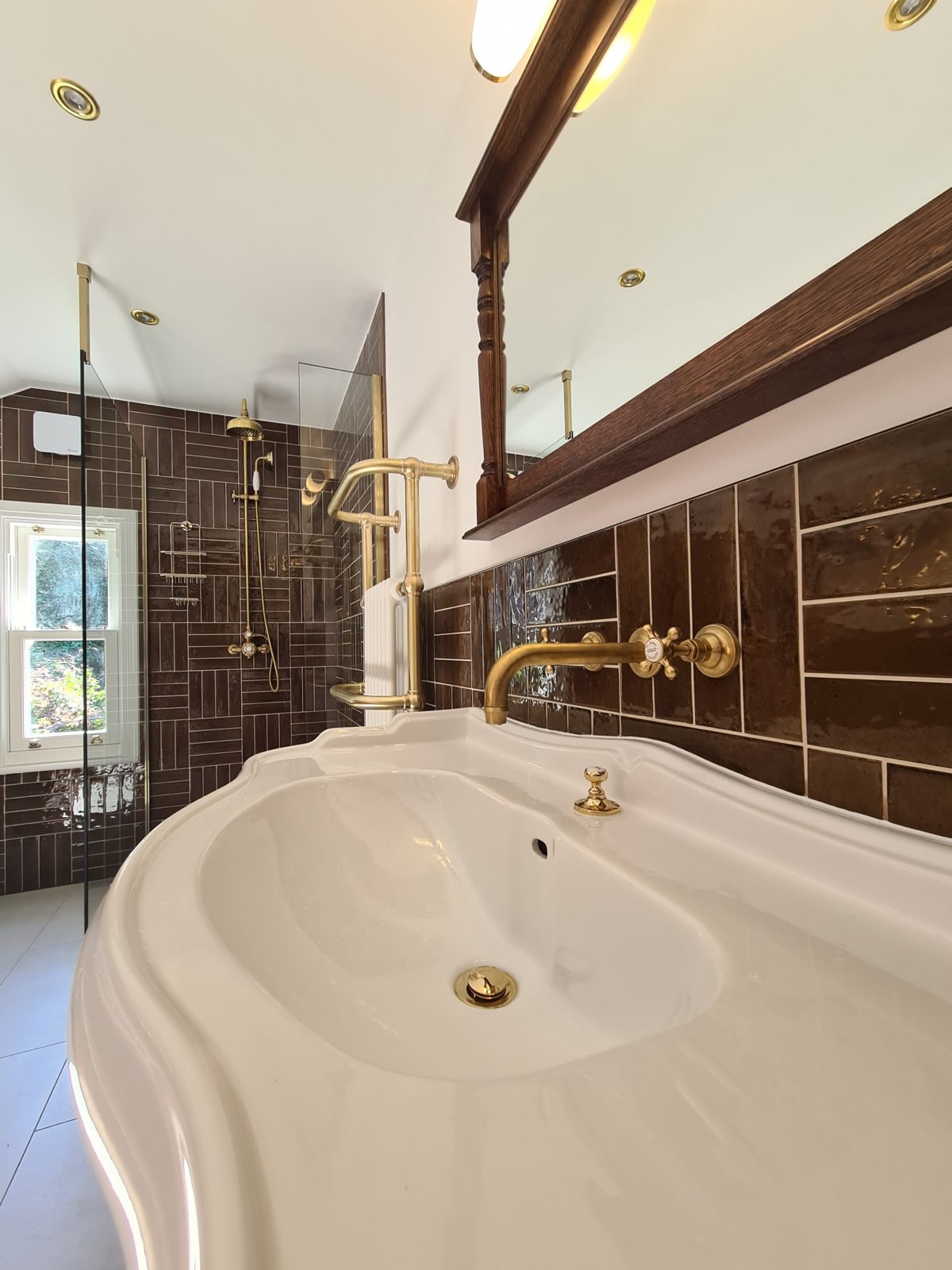 Wall-mounted brass taps over a traditional basin with a timber-framed mirror above, against the same brick-bond wall tiling.
