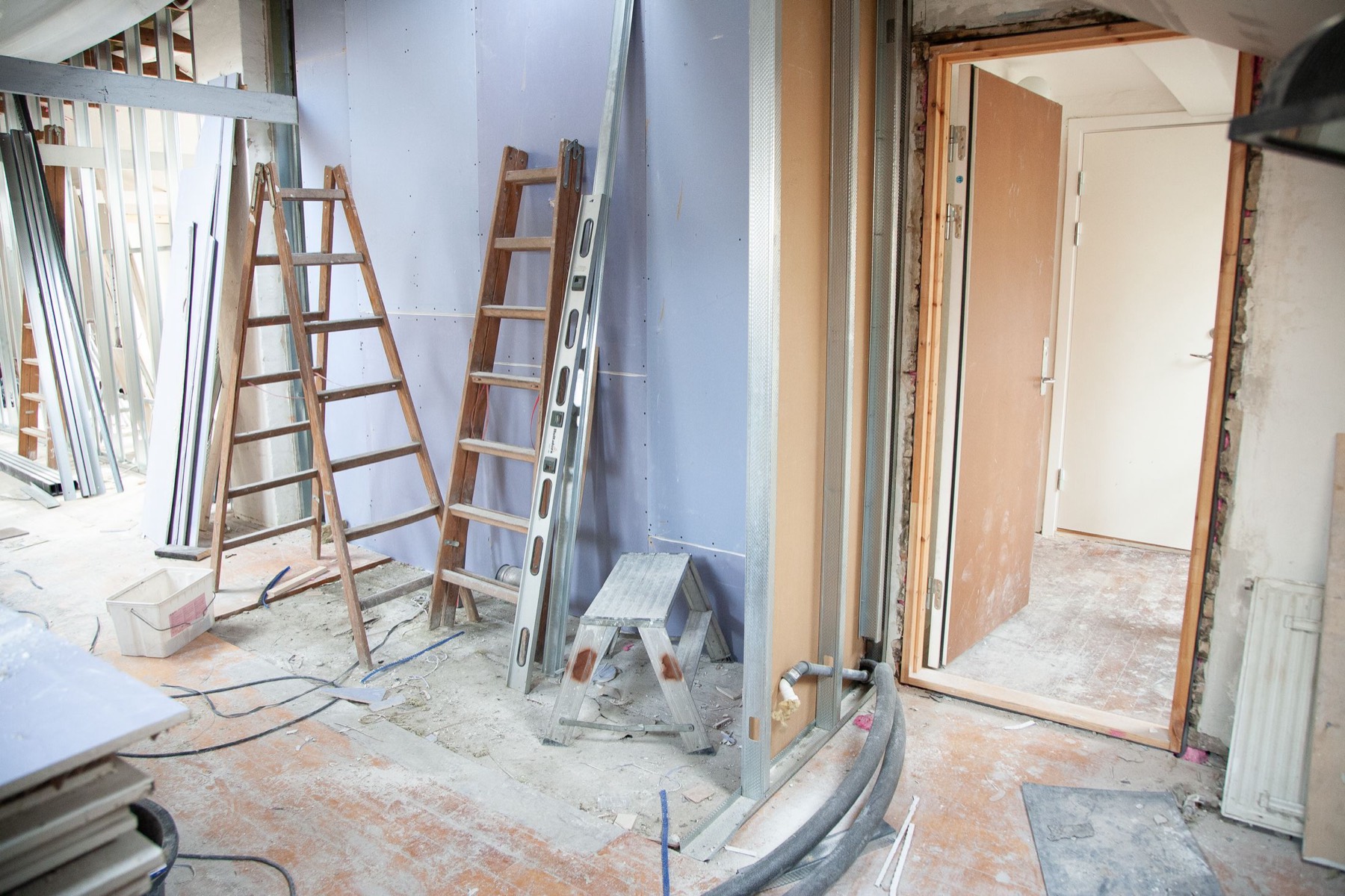 A room stripped back to studs and floorboards mid-refit, with ladders and new stud framing in place